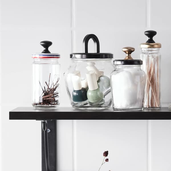 Old jars on a wall shelf that have been reused to store hair pins, nail polish bottles and cotton balls