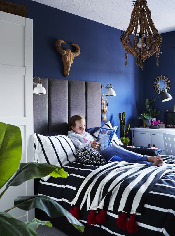 Olivia reading in her bed that has a grey tufted headboard, monochrome bedding and white clamp spotlights on each side.