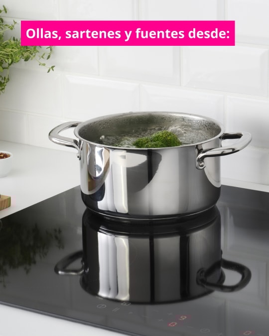 Olla de acero inoxidable con verduras hirviendo sobre una encimera de inducción negra en una cocina blanca. Texto en imagen dice: “Ollas, sartenes y fuentes desde:”.