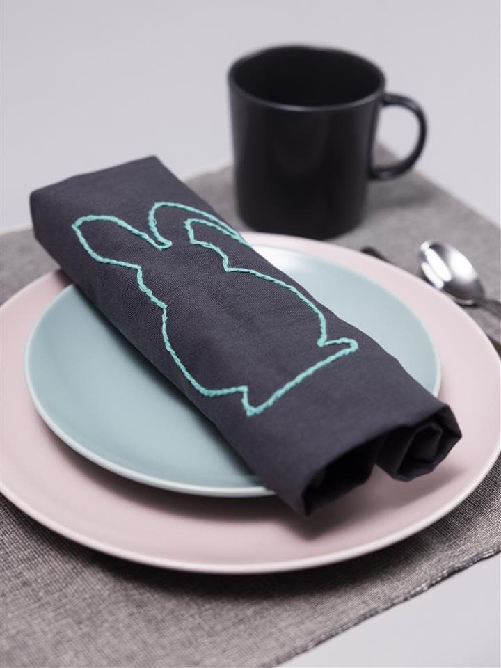 On a blue plate lies a napkin with a rabbit on it, and a black cup in the top right-hand corner.