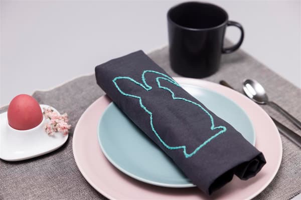 On a blue plate lies a napkin with a rabbit on it, and a black cup in the top right-hand corner.