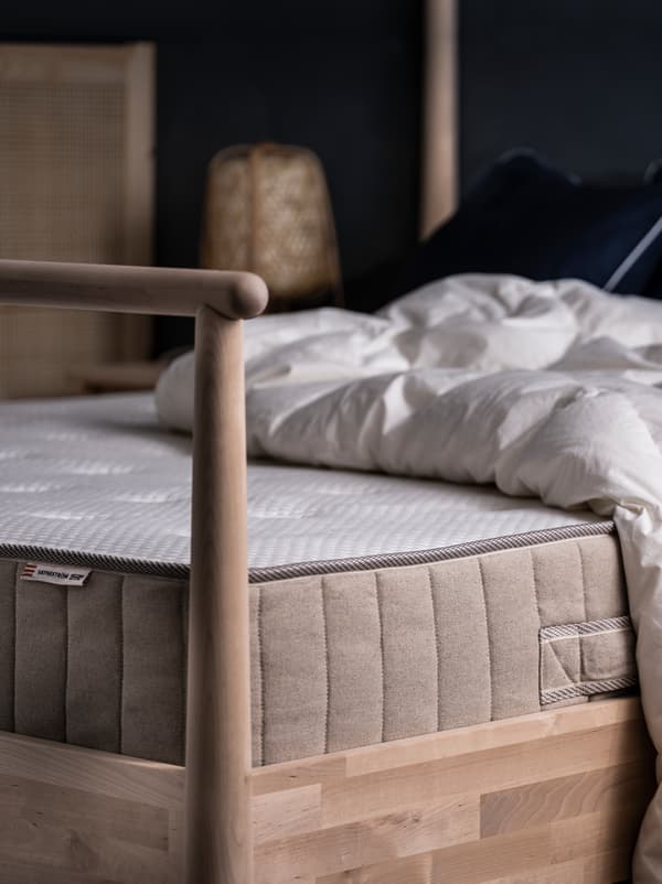 On a GJÖRA birch bed in a softly lit bedroom lie a mattress and a duvet, both without additional bed linen.