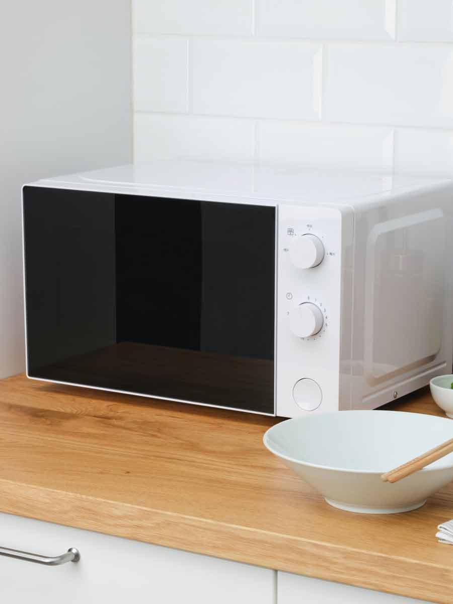 On a kitchen counter, there is a white microwave.