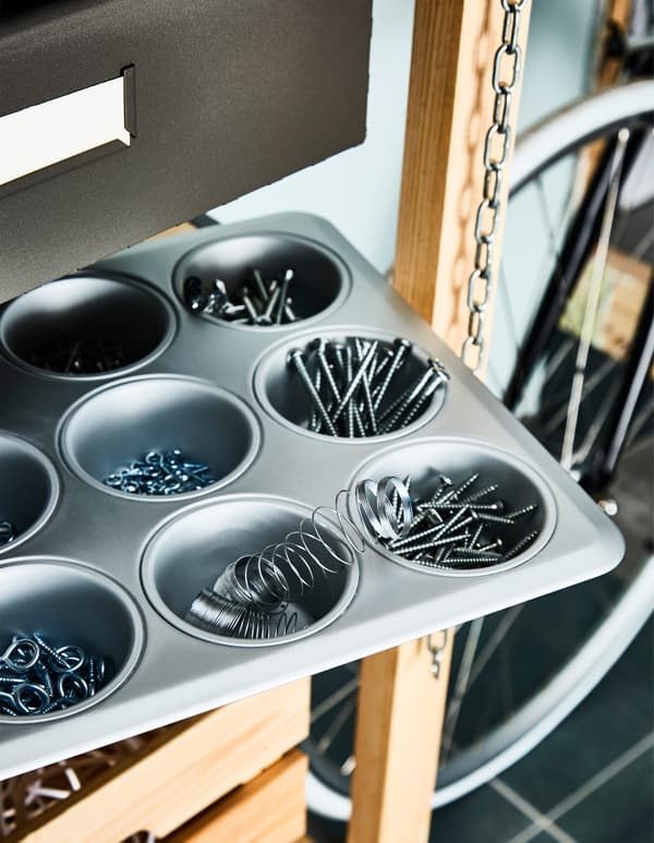 On a shelf in a garage, a muffin tin keeps screws, nails and other hardware organised.