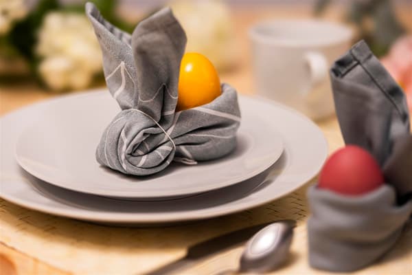 On a white plate sits a rabbit made from a napkin. The napkin has a circle at the back where you can place an egg.