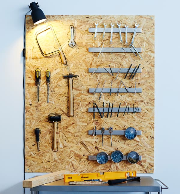 On a wooden board above a work table, several magnetic knife racks hold screw, nails, drill bits and other metal work tools.
