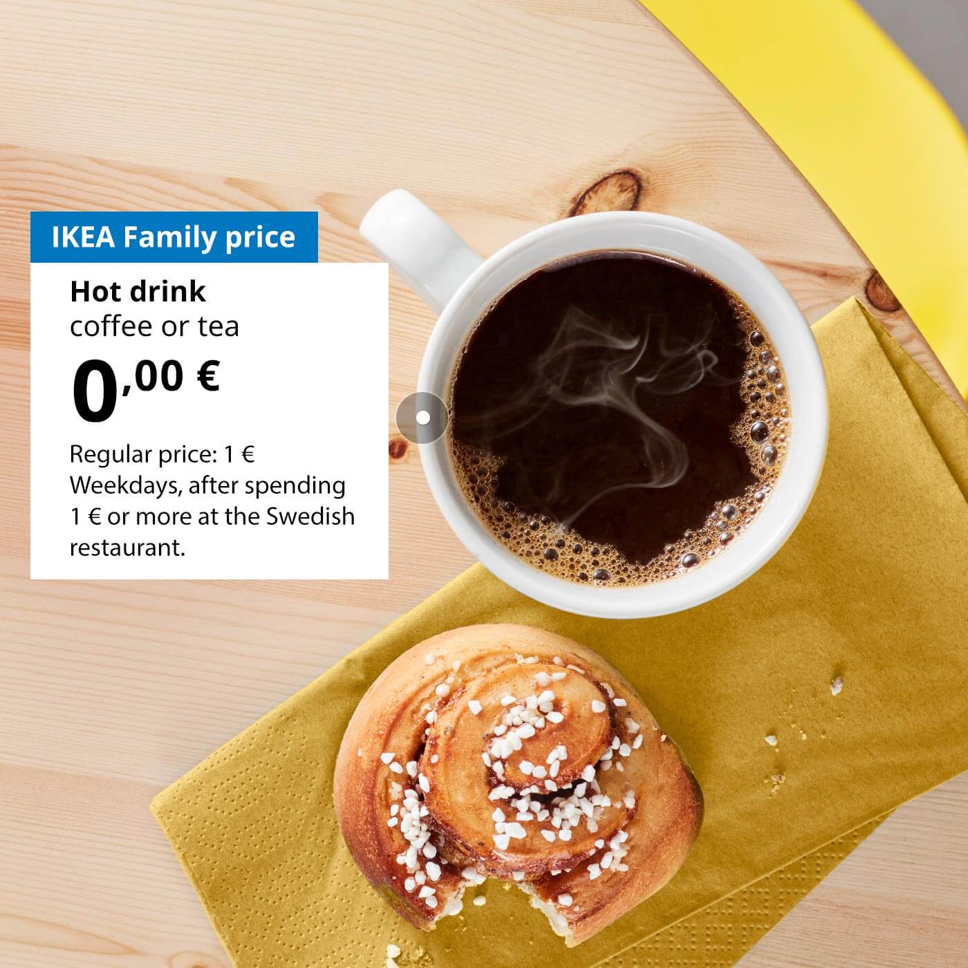 On a wooden table lies a half-eaten cinnamon bun and a mug of coffee. Next to the mug, against a white background, there’s an offer for IKEA Family club members: a hot drink (coffee, tea or cocoa) for 0 €, regular price 1 €.