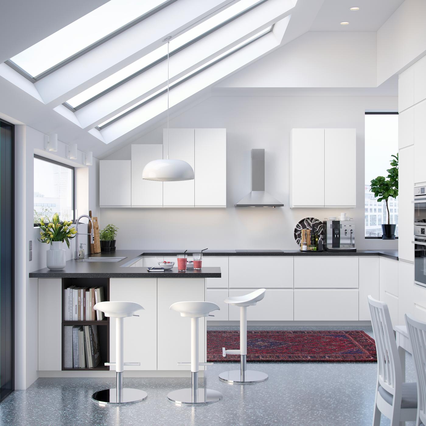 on display is a modern kitchen solution with white fronts and a black worktop, with white bar stools and a red carpet in the centre of the kitchen