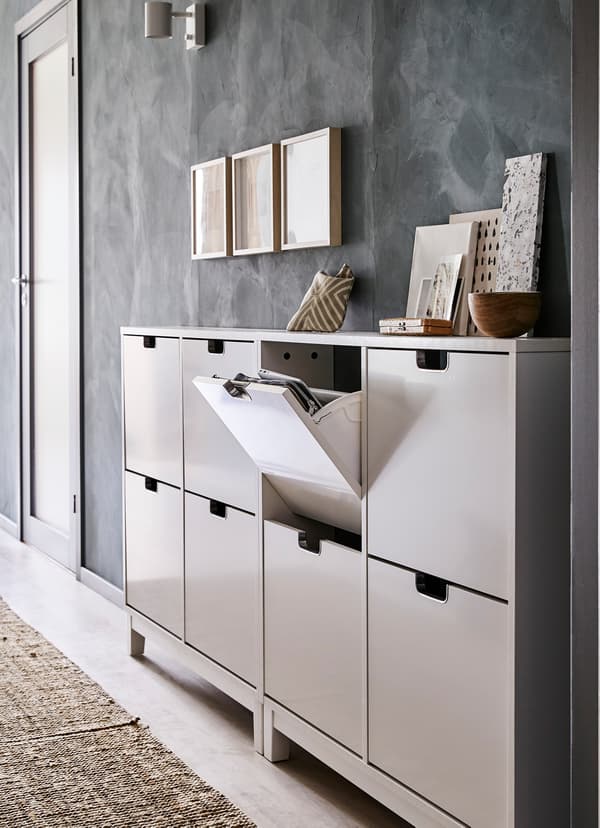 Ondiepe IKEA STÄLL schoenenkast van glanzend wit afgewerkt hout in een smalle gang.