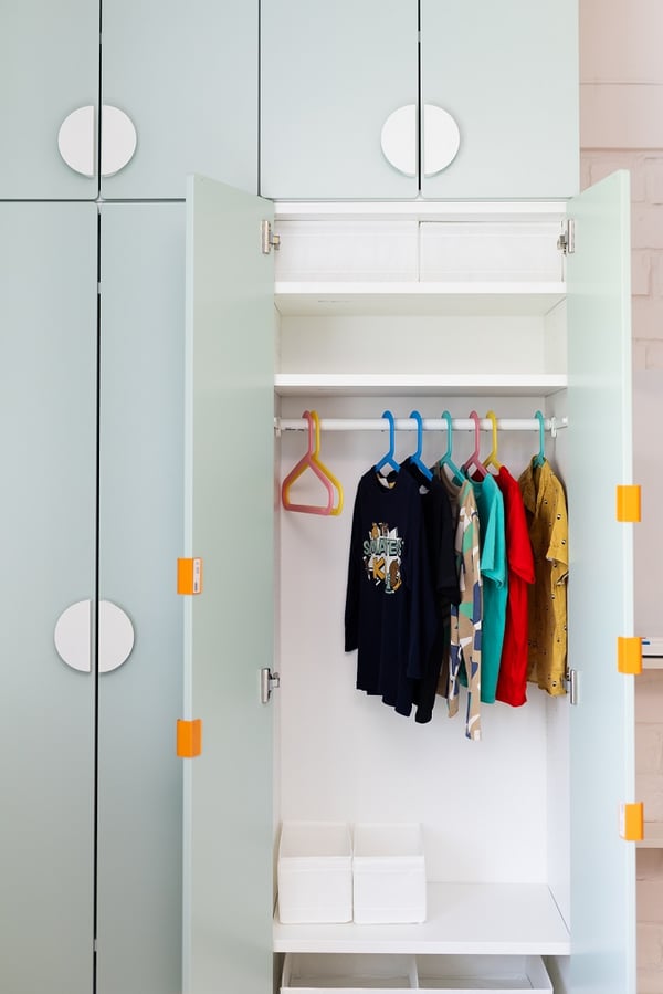 Open children’s wardrobe with hanging clothes, shelves, and storage boxes