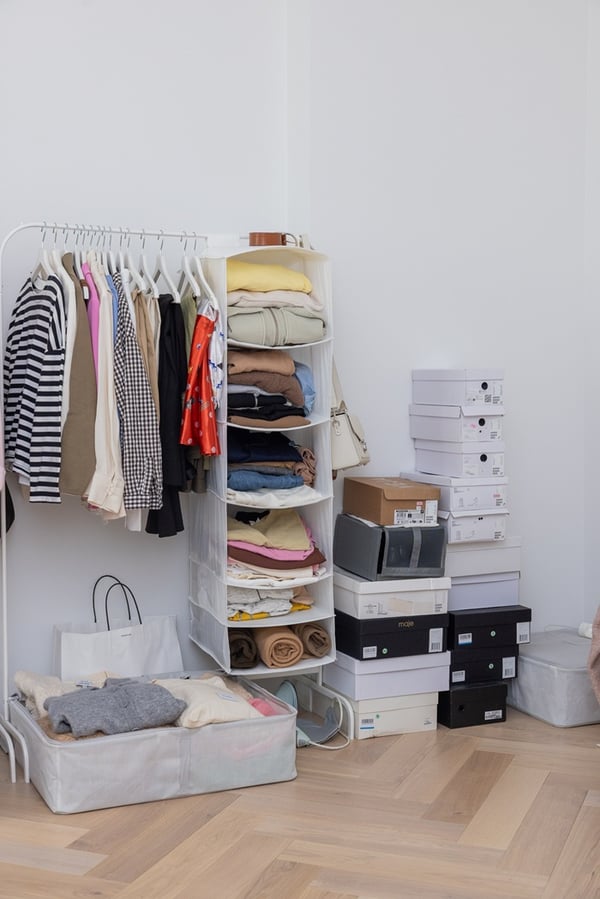 Open clothing storage area with hanging rails, shelves and baskets in a bedroom.
