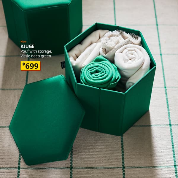 Open deep-green hexagonal storage pouf holds neatly rolled white and teal linens, with its matching lid beside it; a calm, tidy home display with price tag.