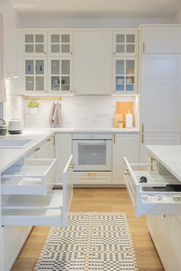 Open drawers in luxury white kitchen with marble surfaces and gold details.