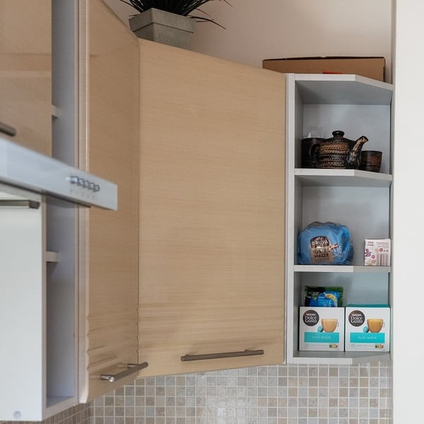 Open kitchen cabinet with shelves displaying coffee capsules and kitchen accessories