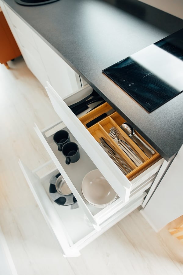 Open kitchen drawers with neatly organized cutlery and dishes – Kitchen storage solution showing utensils, mugs, plates, and cookware in organized pull-out drawers.