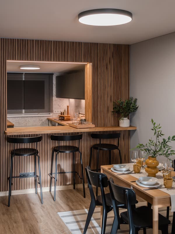 Open-plan kitchen and dining space with wooden decor, a bar with stools, and a round ceiling lamp above.