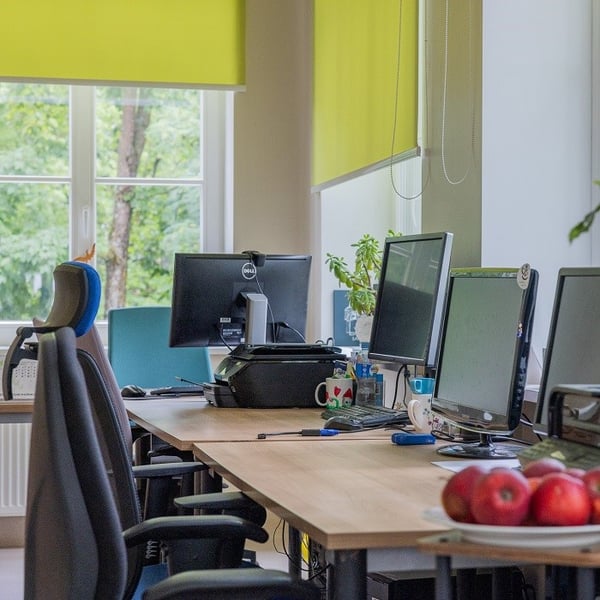 Open-plan office workspace with desks, computers and ergonomic chairs near large windows