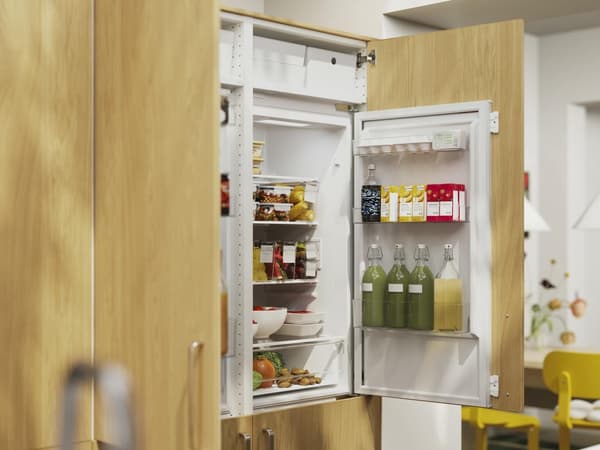 Open refrigerator filled with drinks, produce and packaged foods in a wood-paneled kitchen.
