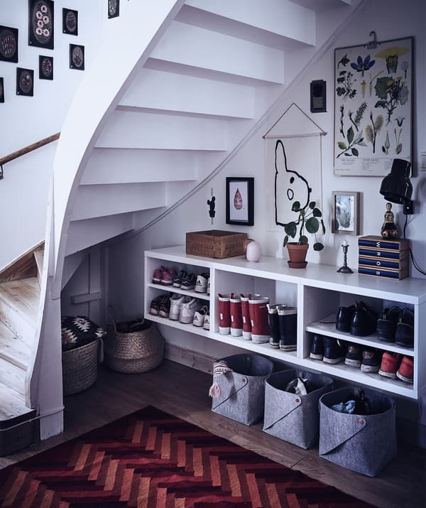 Open under-stairs area with storage baskets and shelves for boots and shoes.