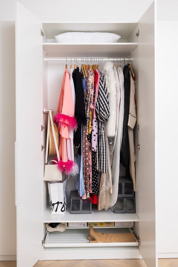 Open wardrobe with hanging rails, shelves and clothes in a bedroom.