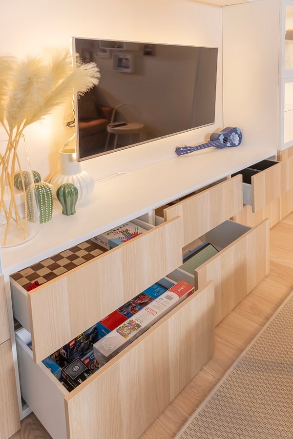 Open wooden drawers under TV unit storing board games and toys.