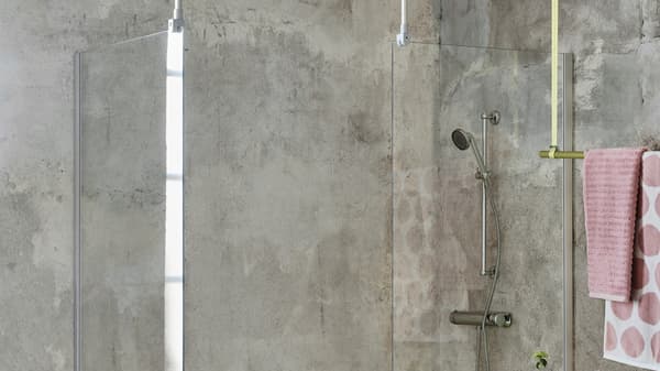 OPPEJEN Duschtrennwände aus Glas vor einer Dusche in Betonoptik. An der Seite des Bildes hängen rosane Handtücher über einter Stange.