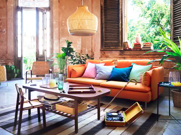 Oranžová pohovka s farebnými vankúšmi vedľa tmavohnedého konferenčného stolíka.