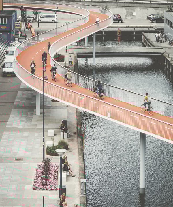 Oranžový most pro cyklisty se vine nad řekou a nábřežím