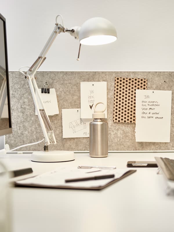 Organiserat skrivbord med vit lampa, grå anslagstavla med to-do-lista, vattenflaska och anteckningsbok med penna.


