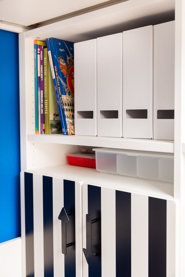 Organized children’s storage unit with books, boxes, and white cabinet doors