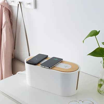 Os cargadores tamén se poden esconder, unha caixa para gardar cables con base de recarga de móbiles con tapa enriba dun escritorio branco.