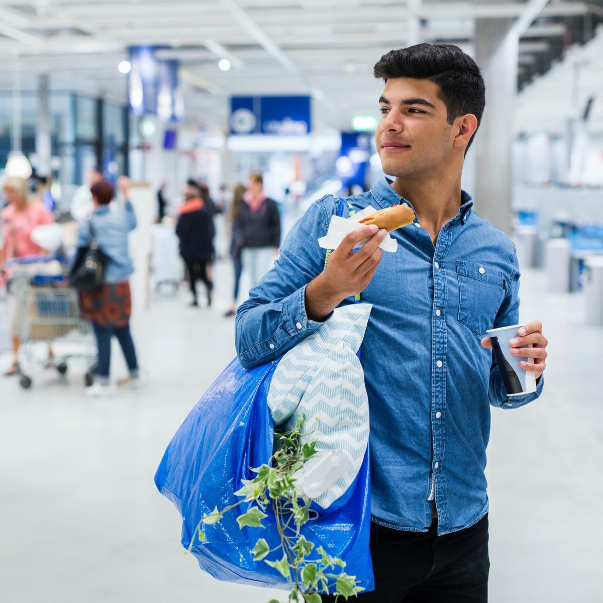 Osoba drži IKEA vrećicu i jede hot dog u IKEA robnoj kući.
