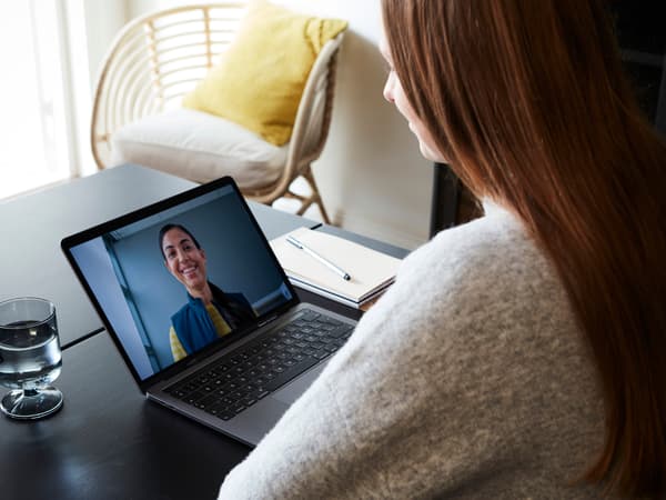 Osoba koristi laptop za video poziv, stolica i jastuk u pozadini.