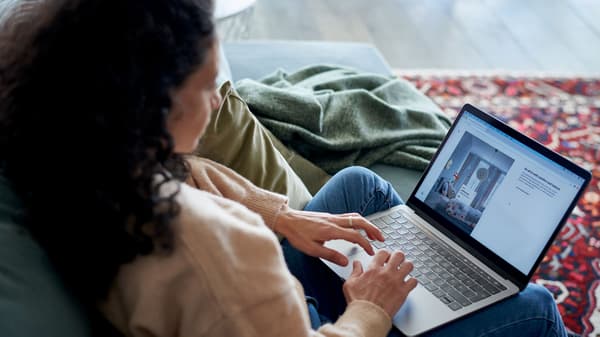 Osoba sjedi na kauču i koristi laptop na kojem je prikazan video poziv.