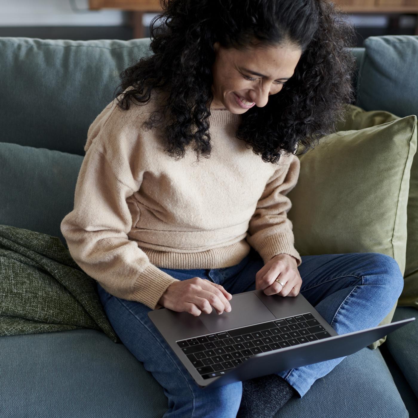 Osoba sjedi na kauču i koristi prijenosno računalo.