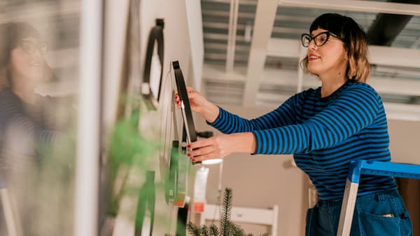 Osoba u plavoj prugastoj majici stoji na ljestvama i postavlja sliku na zid.