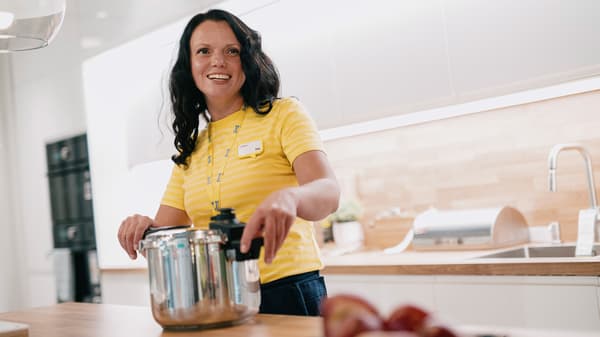 Osoba u žutoj majici drži lonac u modernoj kuhinji.