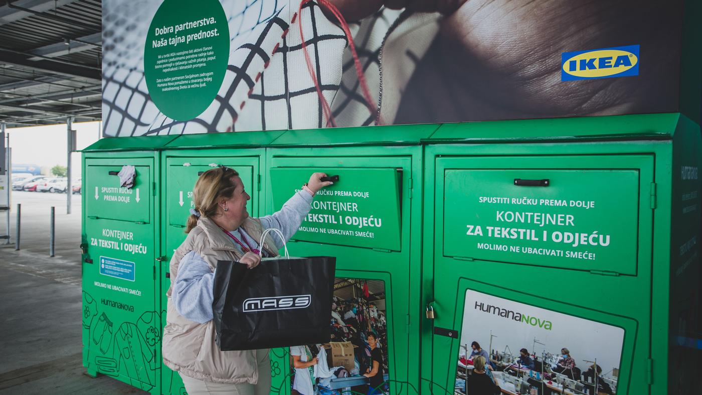 Osoba ubacuje odjeću u zeleni kontejner za tekstil i odjeću ispred trgovine IKEA. Na kontejneru su upute i natpis „Humananova“, a iznad je veliki plakat s porukom o partnerstvu.
