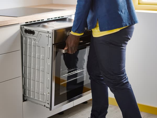 Osoba ugrađuje pećnicu u kuhinjski element, držeći je za ručku dok je gura na mjesto ispod radne ploče.