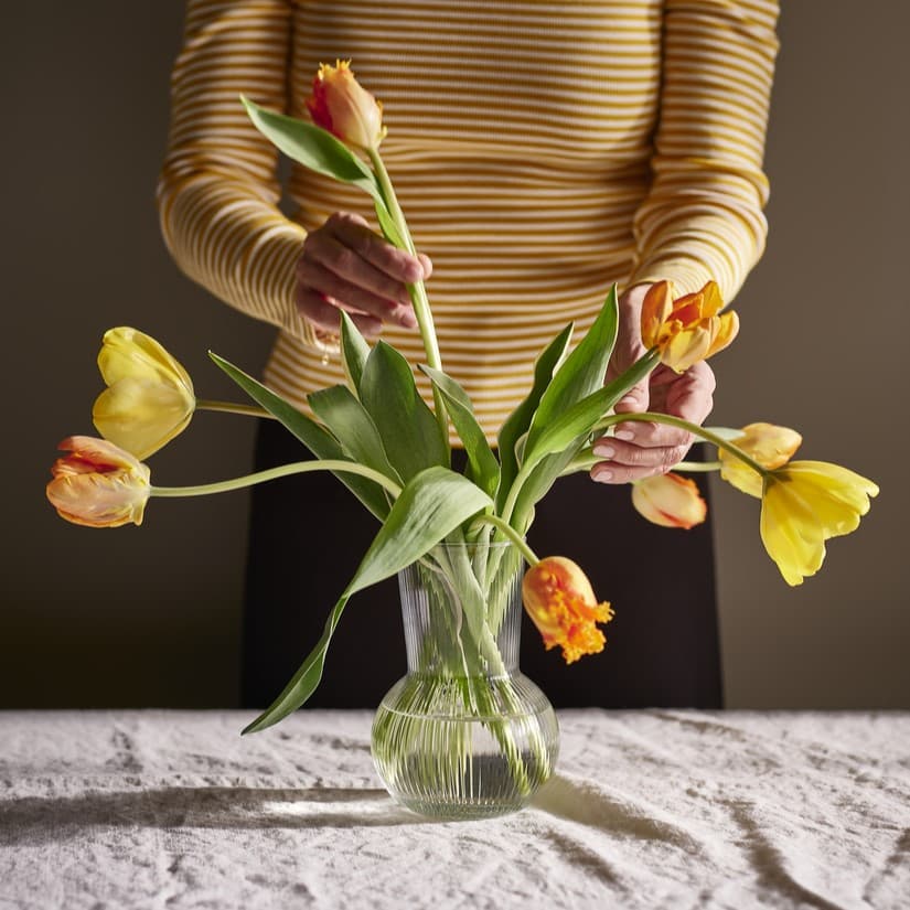 osoba układająca żółe tulipany w szklanym wazonie PÅDRAG z wodą.