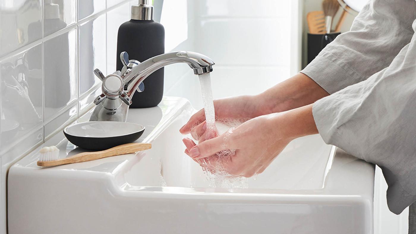 Osoba v sivom župane si oplachuje ruky pod prevzdušneným prúdom vody z batérie RUNSKÄR.