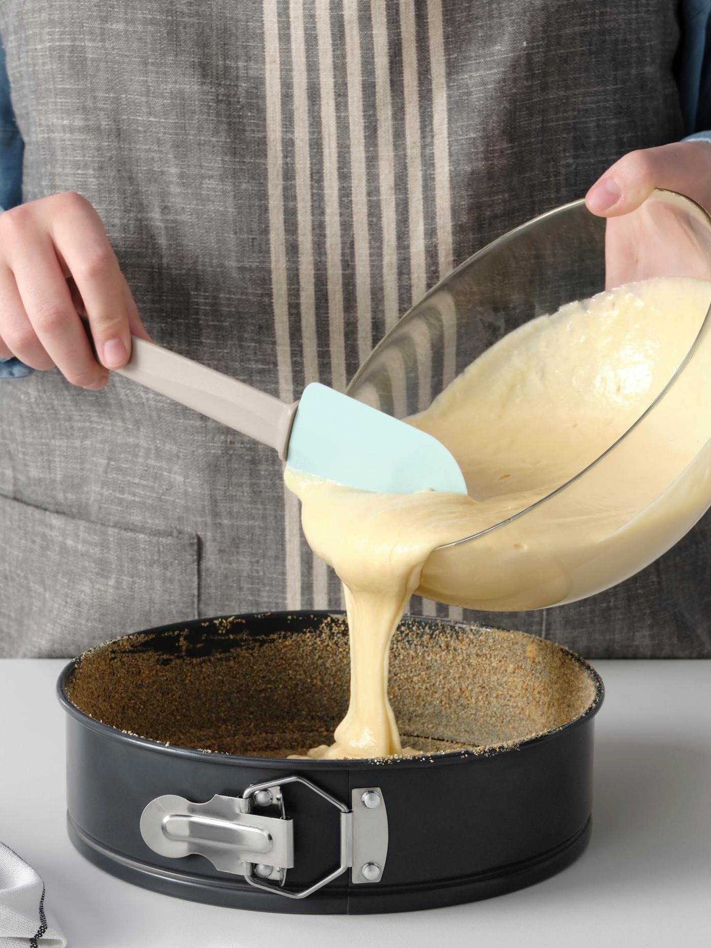 Osoba v zástěře lije těsto ze skleněné misky BLANDA do formy na pečení HEMMABAK.