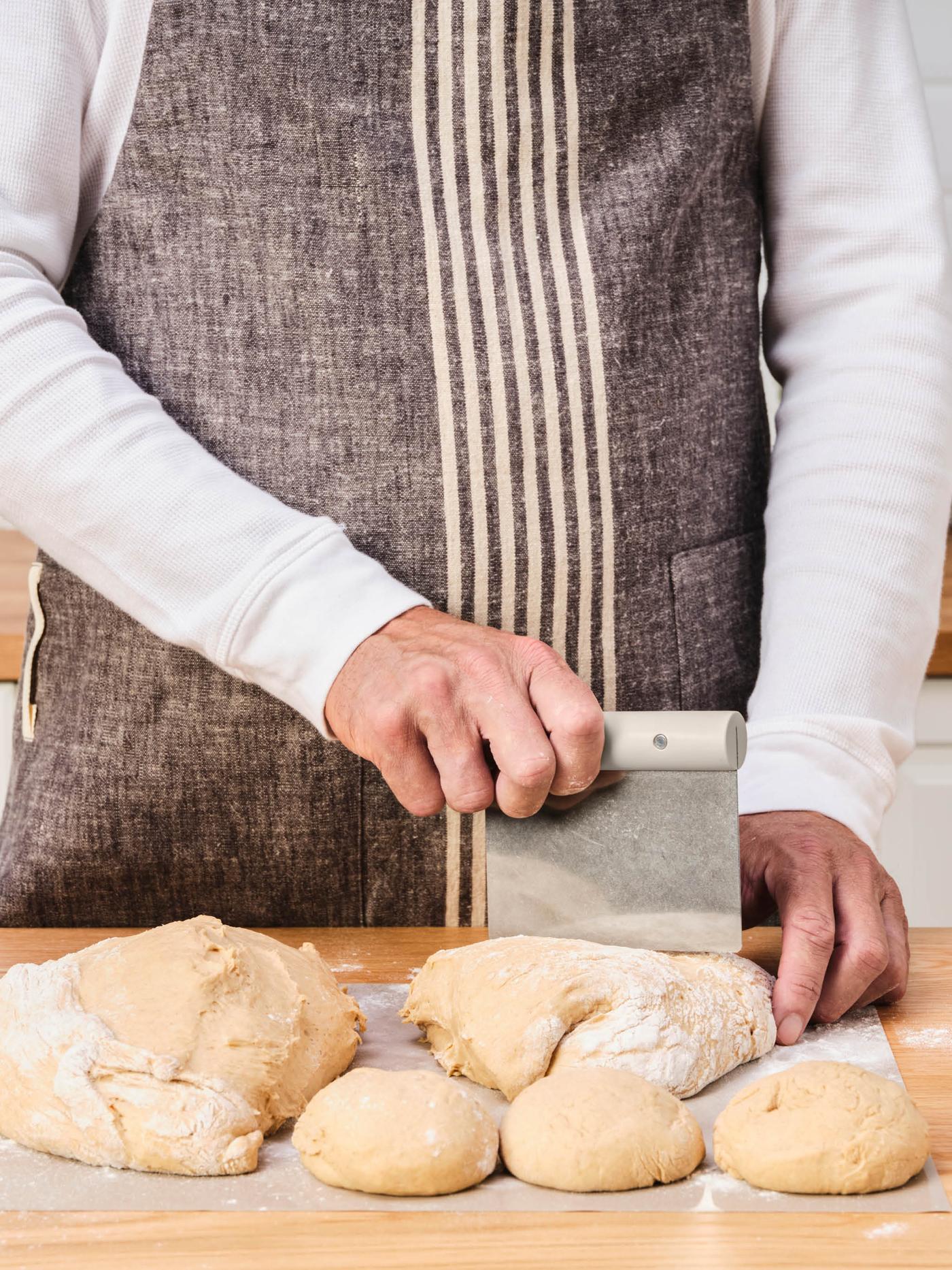 Osoba v zástěře odděluje kráječem LÄTTBAKAD těsto na bochánky.