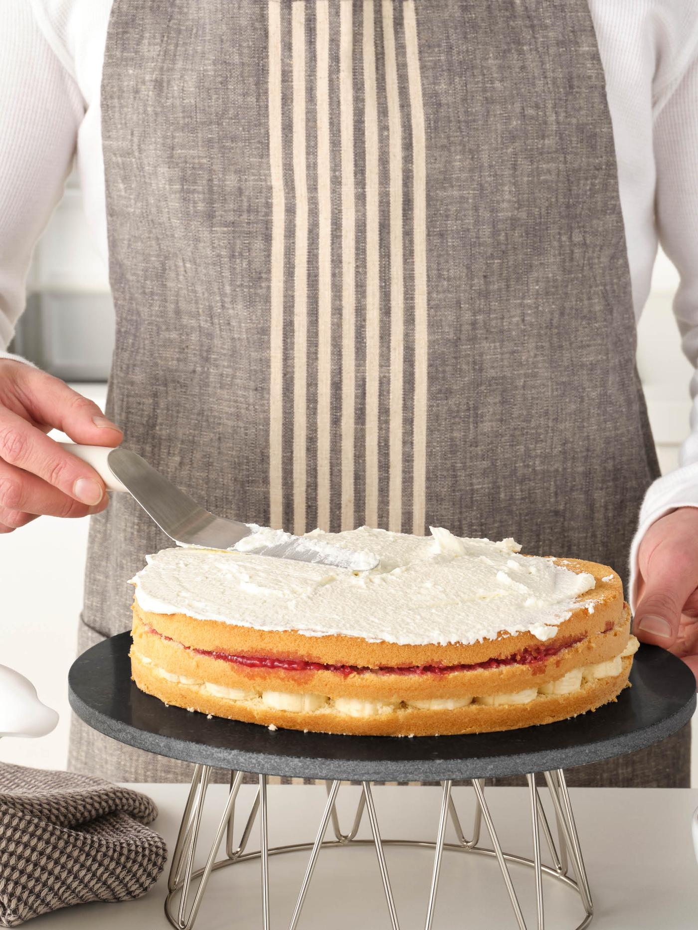 Osoba v zástěře zdobí šlehačkou dort na stojanu BAKGLAD.