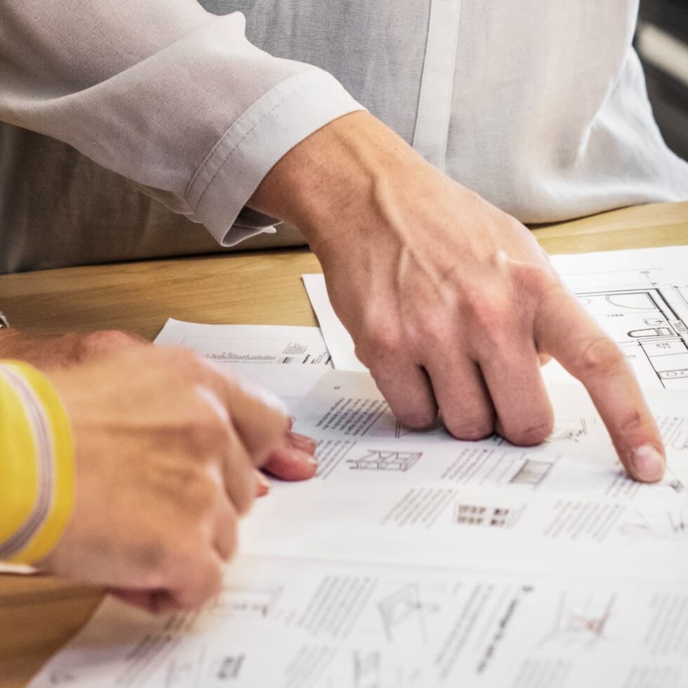 Osobe pregledavaju tehničke nacrte na papiru, jedna osoba pokazuje prstom na dio nacrta.