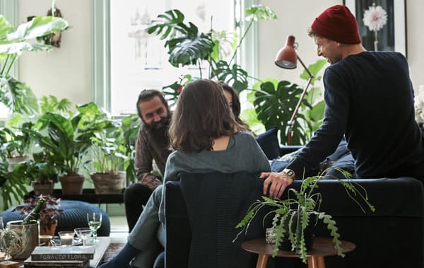 Ospiti seduti su un divano in velluto blu scuro in un soggiorno decorato con piante e tessili a stampa botanica - IKEA