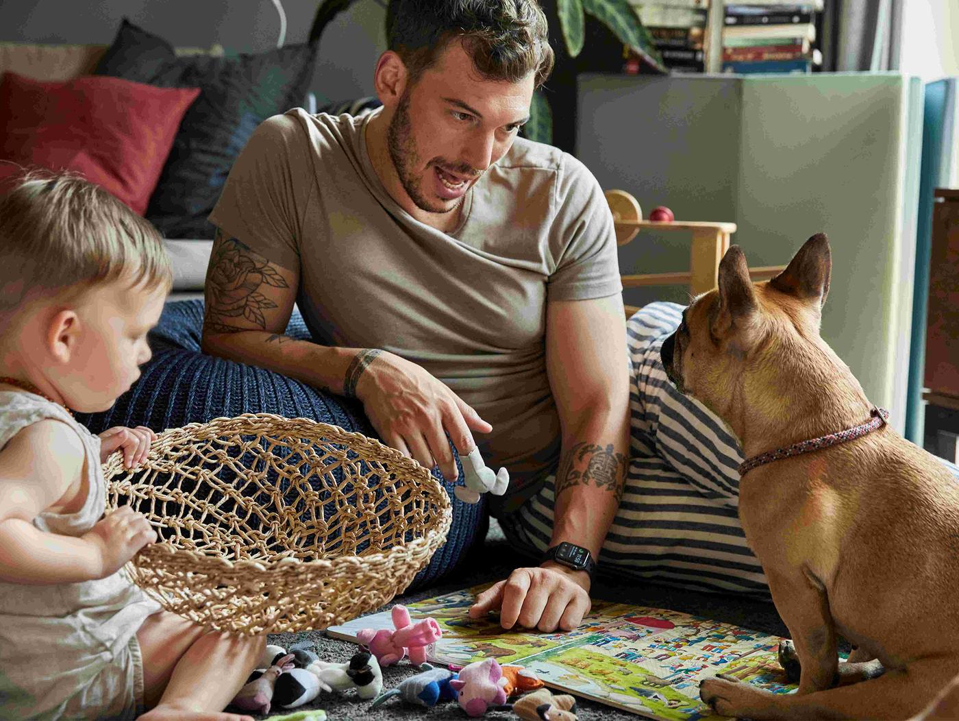 Otac sa detetom i psom sedi na podu i igra se.