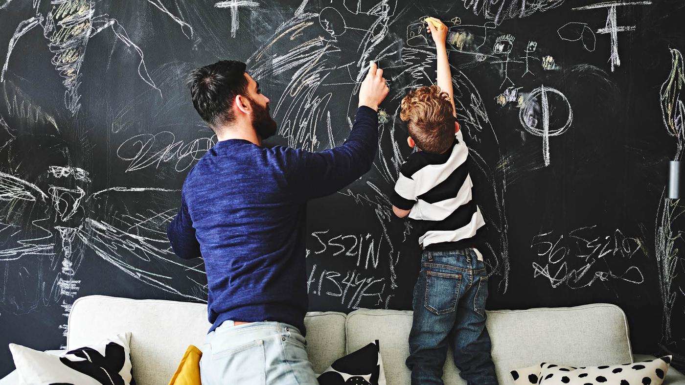 Otec s malým chlapcom kreslia kriedami MÅLA na čiernu stenu.