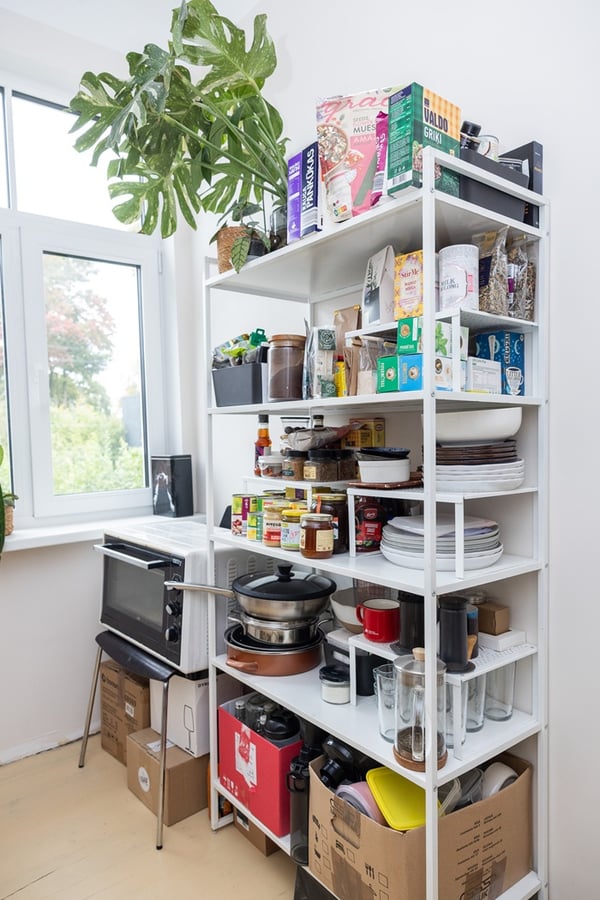 Открытый стеллаж с запасами продуктов и кухонными принадлежностями, используемый как кладовая.