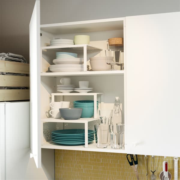 Otwarte drzwi szafki kuchennej, ukazujące białe półki wstawiane VARIERA, które pozwalają w uporządkowany sposób przechowywać talerze, miski i wiele więcej.